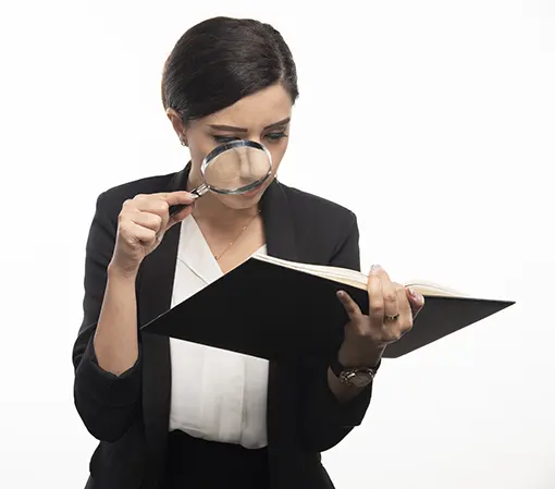 Young brunette female in black suit and white shirt using a magnifying glass to pay attention to tiny details