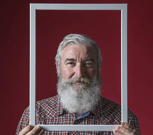 A white Caucasian old man in red striped shirt holding a white photo frame with both hands with his face in the frame