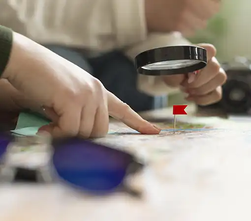 Close up view of a hand holding a magnifying glass and a finger pointing to a tiny red flag