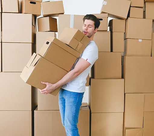 Young energetic man carrying heap of boxes with many other boxes in the background