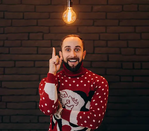 Young man in red sweater smiling brightly pointing up towards a yellow lamp indicating creative idea