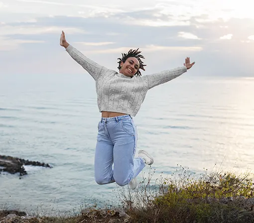 Young white woman jumping in joy because of marvelous experience with sea in background