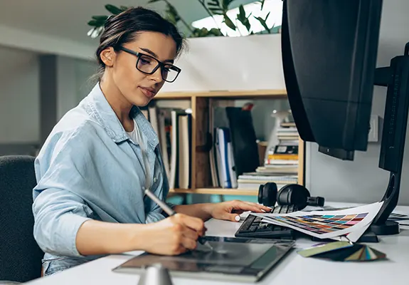 Young woman digital designer focused on her work, using a tablet and computer.